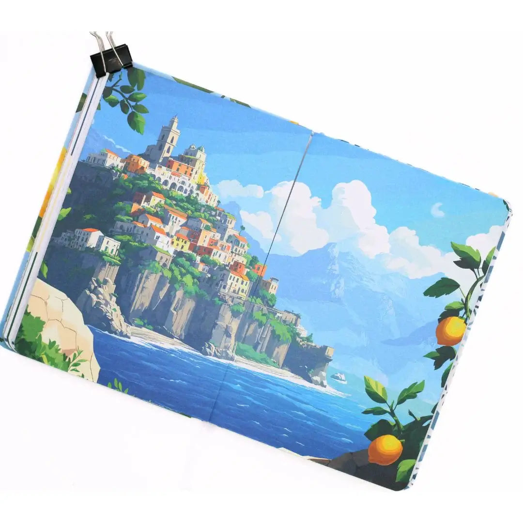 La Dolce Vita Vision Journal open to a scenic illustration of a coastal village with citrus trees.