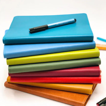 RUSTIK COLOURFUL LEATHER SLIP ON COVER + JOURNAL stacked colorful journals with a blue pen on top.