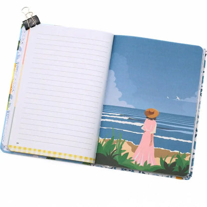 La Dolce Vita Vision Journal open to a page with a serene beach illustration and a woman in a pink dress by the ocean.